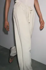 Pantalón culotte color crudo, de tiro medio, cintura elástica ajustable con cordones y bolsillos laterales ocultos en la costura.