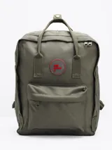 Mochila verde militar con dos asas de mano, dos tiras traseras regulables y un bolsillo frontal con cierre. Tiene un parche circular con letras rojas en el frente.