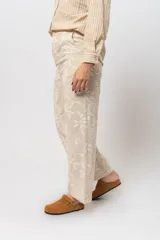 Pantalón de corte recto color marrón con bordado floral blanco.