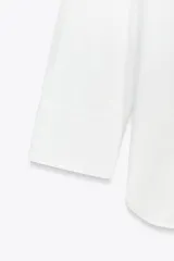 Camisa blanca de corte amplio, con cuello solapa, manga larga y cierre frontal con botones.