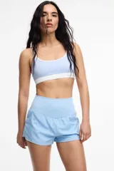 Top deportivo celeste con contorno y tirantes blancos. Presenta copas removibles y el logo de la marca en el contorno inferior.