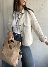 Sobrecamisa color beige con cuello camisero, cierre frontal con botones y bolsillos de parche en el pecho. Presenta detalles de broderie calado en mangas, hombros y bolsillos.