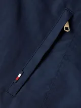 Campera Tommy Hilfiger azul marino con cuello alto blanco, cierre frontal con cremallera, mangas largas y cinturón ancho de tela del mismo tejido para ajustar en la cintura.