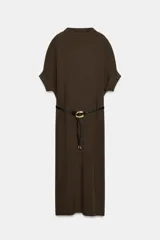 Vestido negro de tejido de punto, corte midi y silueta holgada, con cuello alto acanalado y mangas cortas tipo murciélago. Se ajusta a la cintura con un cinturón fino de efecto piel negro con hebilla dorada en forma de C.