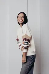 Sweater de punto color crema con cuello redondo y mangas largas con diseño geométrico en tonos beige, rojo, azul y blanco.