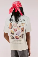 Remera blanca de algodón con cuello redondo y estampado pequeño en el pecho con la frase "Treasures of the Tides" y un dibujo de una concha. Corte holgado.