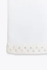 Top blanco de punto elástico con cuello redondo y sisa. Detalle de aplicación de crochet a contraste.