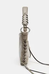 Bolso de hombro color gris topo, con formato rectangular y asa corta. Presenta dos bolsillos frontales con cierre de cremallera y detalle de tiras colgantes. El asa es de cuero trenzado con herrajes metálicos.
