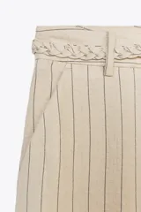 Pantalón de tiro alto color beige con finas rayas verticales negras, pernera ancha y cinturón trenzado a tono.