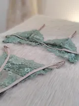 Conjunto de lencería de encaje floral color verde menta, con detalles y tiras ajustables en tono beige/tostado. Incluye un corpiño triangular sin aro y una bombacha tipo colaless o tanga.