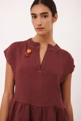 Vestido corto de lino color vino tinto, con escote en V y mangas cortas tipo musculosa. Presenta un corte holgado con volados en el ruedo.