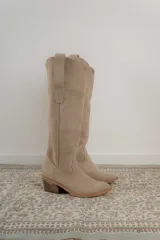 Bota alta de cuero color beige, estilo texana, con caña alta y taco bajo.
