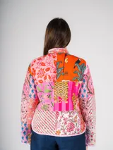 Chaqueta con cuello alto y botones tipo nudo, confeccionada con la técnica patchwork, combinando retazos de telas tradicionales con bordados y estampados vibrantes que mezclan flores, formas geométricas y cultura textil.