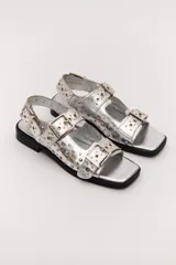 Sandalias bajas color crema con apliques de tachas metálicas y hebillas plateadas.