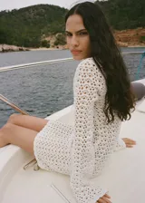 Vestido corto de crochet color blanco, con cuello en pico, mangas largas y cierre de lazo en la parte delantera.