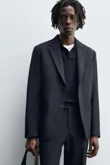 Blazer negro de lana con cuello de solapa de muesca, manga larga con puños abotonados, bolsillos de vivo en el pecho y de solapa en la cadera, bolsillo interior, aberturas en la espalda y cierre frontal con botones.