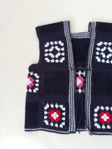 Chaleco sin mangas, confeccionado con cuadrados de cuero negro perforado combinados con cuadrados de crochet en hilo de algodón negro y blanco, con detalles centrales en rojo.