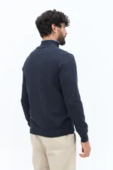 Sweater de tejido liso color verde oscuro, con cuello medio y cierre frontal parcial plateado. Presenta puños y cintura acanalados, y un pequeño logo bordado en el pecho.