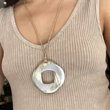 Collar largo con cordón de cuero color beige y dije circular de asta esmaltada en tonos beige, blanco y plateado.