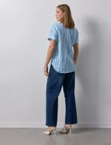 Blusa de algodón estampado a rayas verticales en tonos celeste, azul y verde. Tiene cuello a la base, escote en V con bordado y botones. Terminación de ruedo con nudo.