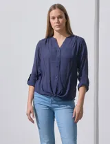 Blusa blanca de gasa marca Zac & Rachel, con cuello a la base, escote en V, abertura central con botones, bolsillo aplicado en el pecho y mangas largas regulables con presilla y botón. Tiene terminación opcional de nudo en el ruedo.
