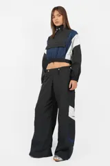 Buzo rompevientos anorak gris, de cuello alto, silueta boxy fit, con elástico en terminación de cintura y mangas. Detalle de recortes a contratono. Cierre centrado en delantero de acceso. Bolsillo con tapa por debajo, con cierre escondido. Tancas en cuello con elástico en su contorno, por interior. Estampa en lateral derecho, y centrado en espalda.