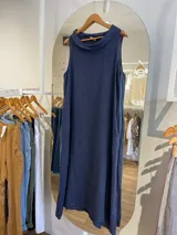 Vestido largo sin mangas color azul claro, confeccionado en lino, con cuello tipo buche o drapeado. Presenta un calce holgado y bolsillos laterales.