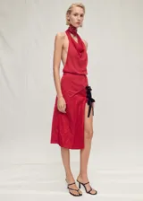 Top rojo de punto fino con cuello halter drapeado y espalda descubierta. Presenta cierre de botones en el cuello, bajo asimétrico y cinturón tipo lazo en la cintura.