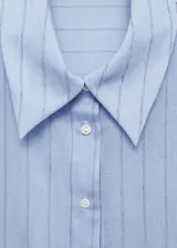 Camisa celeste con rayas verticales finas, de tejido fluido, manga larga abotonada, cuello camisero y corte recto.