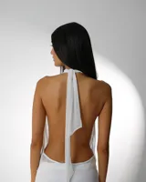 Vestido blanco de microtul premium, con escote halter profundo y drapeado en el busto. La prenda es ajustada en la parte superior y presenta un pantalón ancho y transparente debajo.