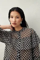 Camisa negra semitransparente de encaje bordado con diseño geométrico. Tiene silueta fluida, mangas largas y volados en el frente y los hombros.