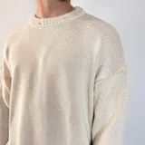 Sweater tejido color crema con cuello redondo y terminaciones con efecto desgastado y roturas.