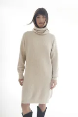 Vestido tipo sweater color beige, de tejido de punto acanalado, corte recto, largo a la rodilla y cuello alto.