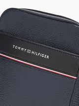Bandolera Tommy Hilfiger de poliuretano granulado color azul marino, con correa ajustable de tejido jacquard con el logo de la marca. Tiene un compartimento principal con cierre, bolsillo interior con cremallera y bolsillo exterior abierto.