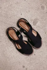 Sandalia plana de color tostado confeccionada en una combinación de neopreno y cuero. Posee un diseño de tira ancha con aberturas sobre el empeine, plantilla acolchada y suela de goma con costuras a la vista.