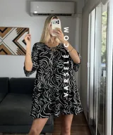 Vestido corto color verde oliva con estampado de hojas en blanco y negro, escote con lazo ajustable y mangas 3/4 acampanadas.