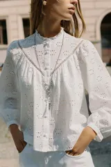 Camisa blanca de manga larga con cuello con volantes y bordados perforados. Cierre frontal con botones a tono.