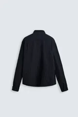 Camisa negra con finas rayas verticales blancas, de corte holgado, manga larga y cuello abotonado.