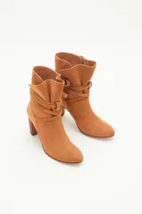 Botas de caña media de gamuza negra, con taco cuadrado y punta fina. Presenta tiras terminadas con borlas que se cruzan y atan alrededor de la caña.