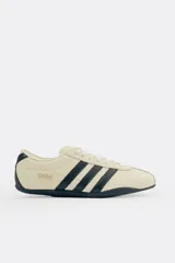 Championes Adidas Tokyo color crema con detalles en negro, con las tres tiras características de la marca en los laterales.