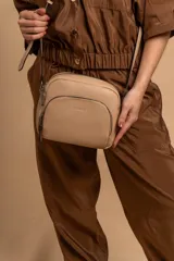 Bandolera de cuero sintético color beige, con diseño compacto y elegante. Cuenta con un bolsillo frontal con cierre y un compartimento principal con cierre. La correa es regulable.