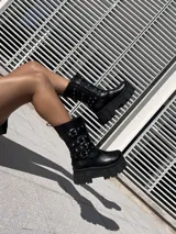 Bota negra de ecocuero con caña media, plataforma track y tres correas con hebillas plateadas.