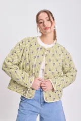 Chaqueta acolchada color verde claro con rayas verticales y pequeños estampados florales en tonos azules y verdes. Tiene cuello redondo, cierre frontal con botones y ribetes de color crudo.