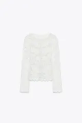 Top blanco de encaje con bordados florales, cuello redondo y mangas largas.