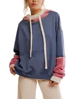 Hoodie oversized color azul desgastado con capucha y bolsillo canguro. Presenta un cuello y puños de tejido de punto con patrón a rombos en rojo y blanco, y cordones gruesos de color crema.