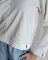 Remera blanca de mangas largas con cuello en V y costuras a la vista.