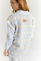 Chaleco tejido de lana con patrón de rombos en tonos lila, rojo y beige, con cuello en V y ribetes en color crema. Diseño oversize.