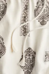Pantalón de corte holgado en tejido liviano de mezcla de lino y viscosa, color crudo con estampado paisley en marrón. Modelo con cintura elástica fruncida y cordón para ajustar, bolsillos laterales discretos y piernas rectas con bajo deshilachado.