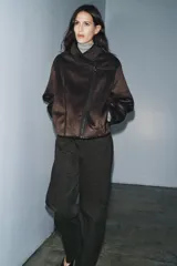 Cazadora de estilo aviador con cuello subido, manga larga y cierre frontal asimétrico con cremallera. Presenta un diseño de doble faz con exterior de efecto ante y forro interior de borreguillo a tono, con detalles de ribetes en cuero sintético.