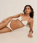 Conjunto de bikini blanco con ribete marrón en contraste. El corpiño es de corte triangular con detalle de argolla en el centro. La bombacha es de corte clásico con tiro medio.